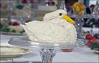 A marzipan swan sits in front of a colorful tower of fruits and sweets on a banquet table.