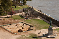 The eastern corner of the 1608 church excavation sits behind a statue of John Smith, an experimental “barracks” in the background.